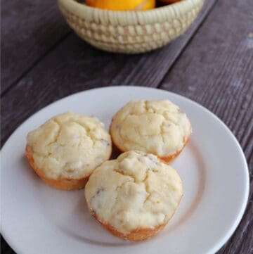 3 lemon nut muffins on a white plate with a basket of fresh meyer lemons behind it.