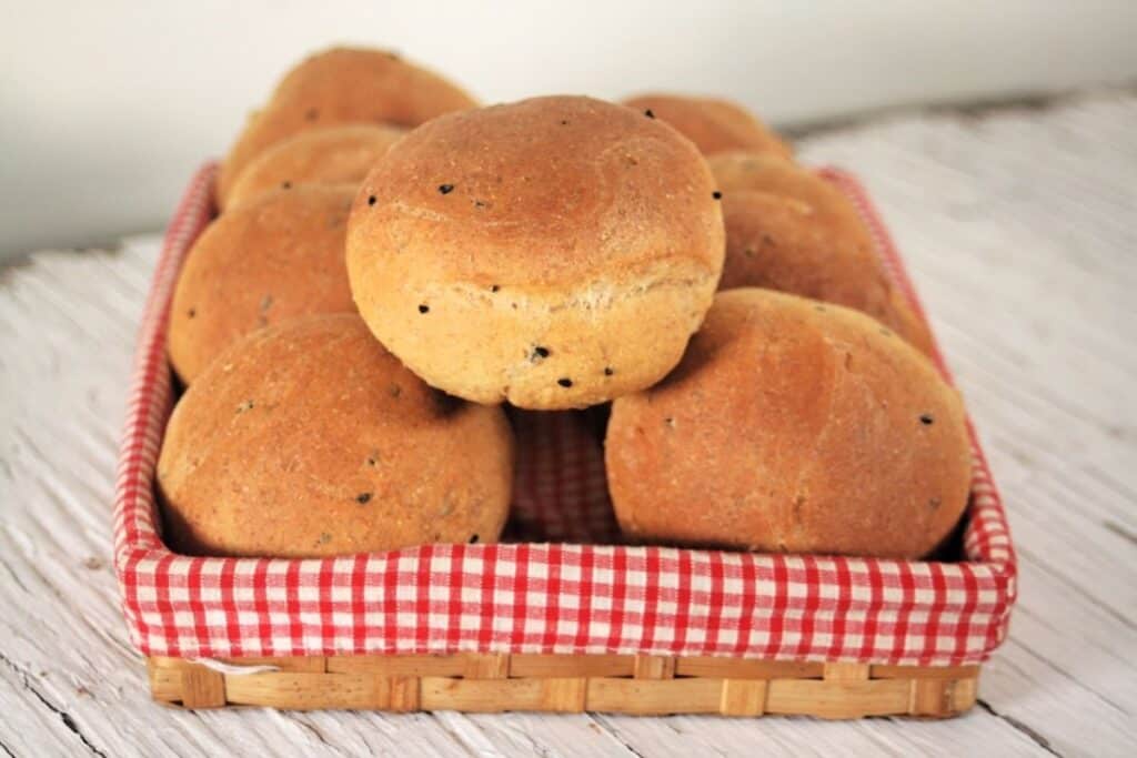 Pumpernickel rolls stacked inside a red & white checkered lined basket.