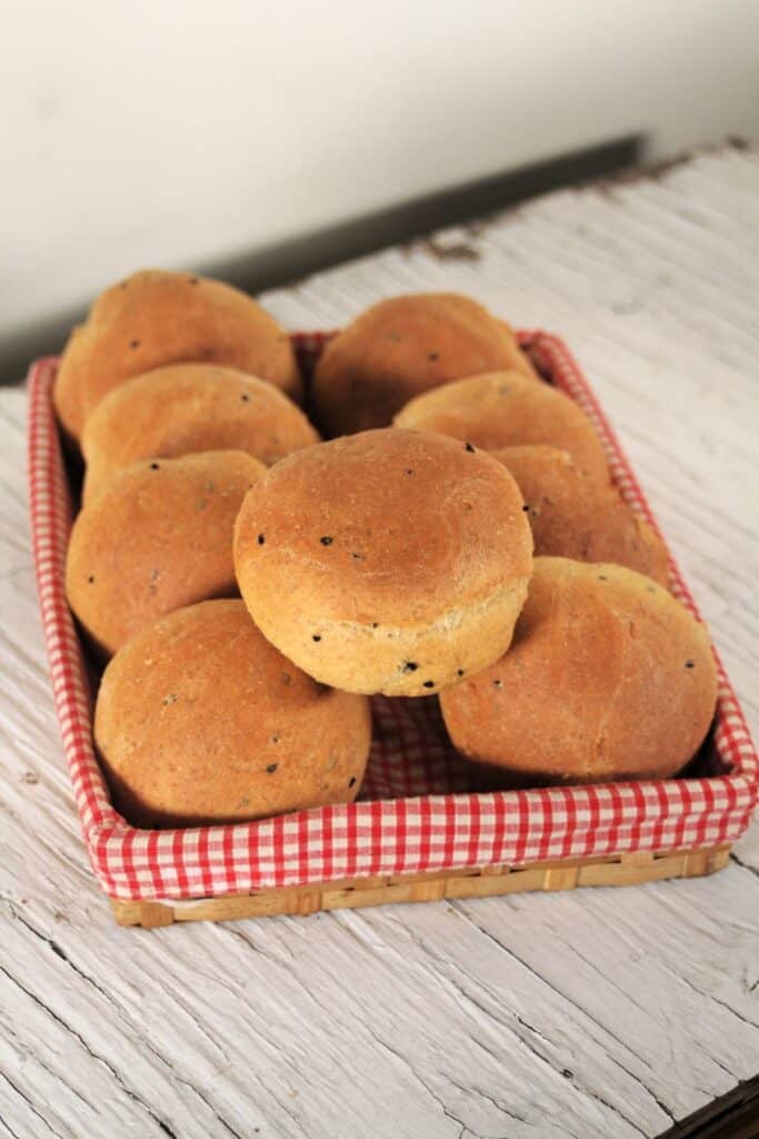 Pumpernickel rolls stacked inside a red & white checkered lined basket.