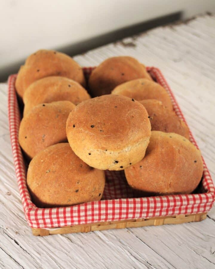 Pumpernickel rolls stacked inside a red & white checkered lined basket.