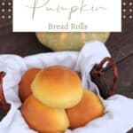 A white napkin lined basket full of pumpkin dinner rolls sitting in front of a green and orange striped pumpkin with text overlay stating: Pumpkin Bread Rolls.