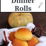 A white napkin lined basket full of pumpkin dinner rolls sitting in front of a green and orange striped pumpkin with text overlay stating: Pumpkin Dinner Rolls.