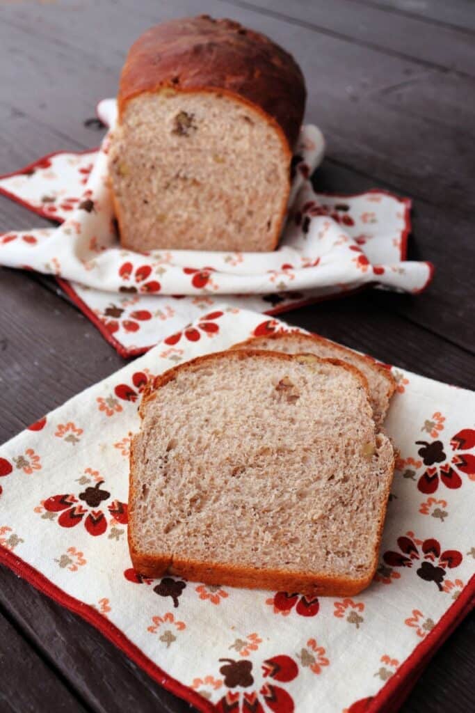 Slices of walnut bread sitting on a napkin with remaining loaf behind them also sitting on a napkin.