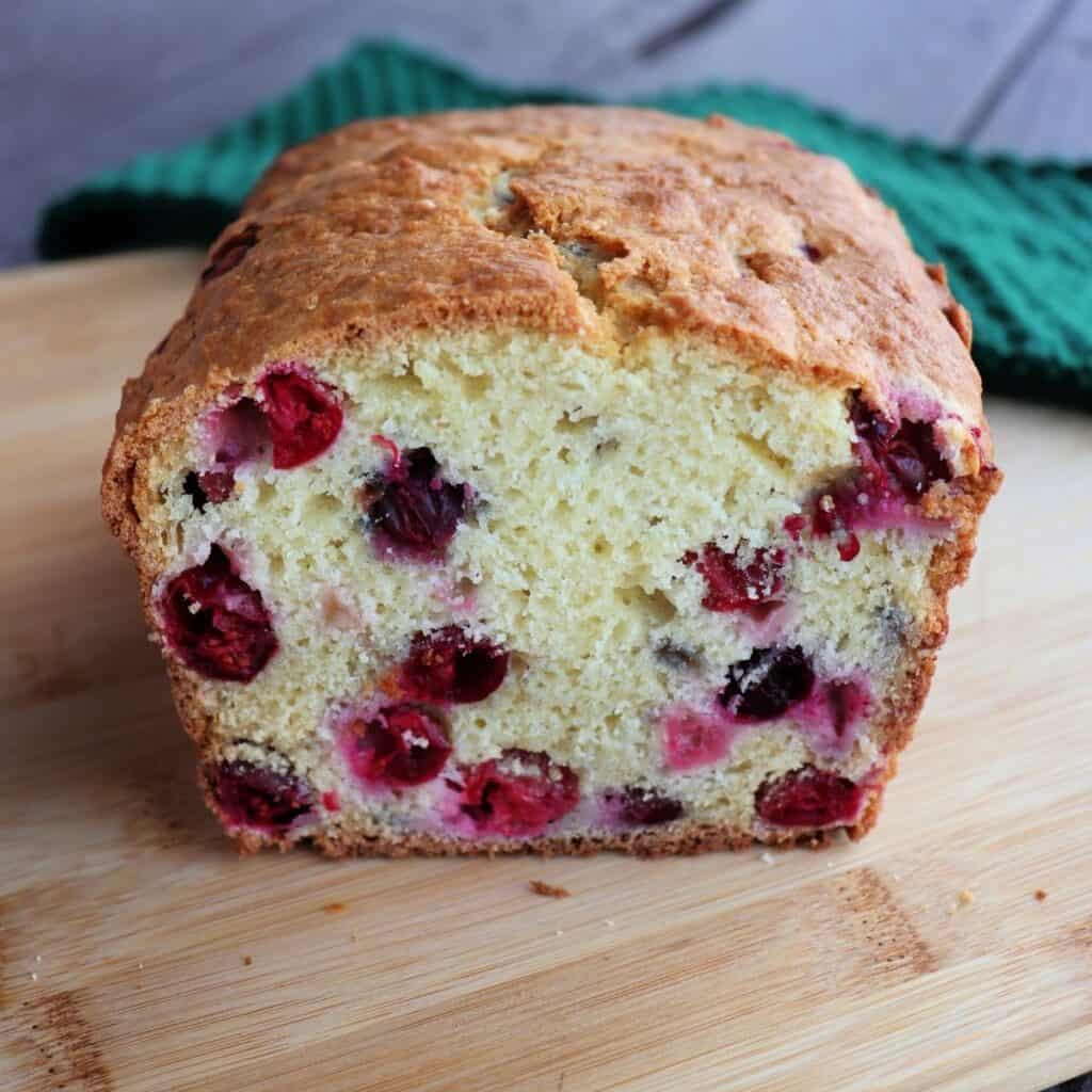 A loaf of cranberry quick bread with the end cut off exposing the berries inside the bread.