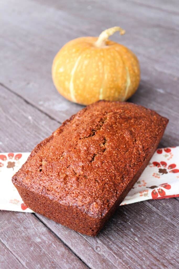 A loaf of pumpkin whole wheat nut bread sitting on a napkin with a pumpkin in the background.
