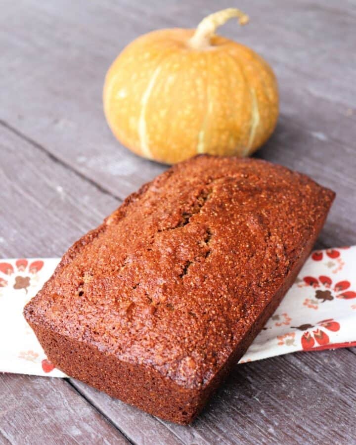A loaf of pumpkin whole wheat nut bread sitting on a napkin with a pumpkin in the background.