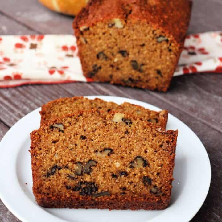 2 slices of whole wheat pumpkin bread on a white plate with rest of loaf sitting on a napkin in the background.