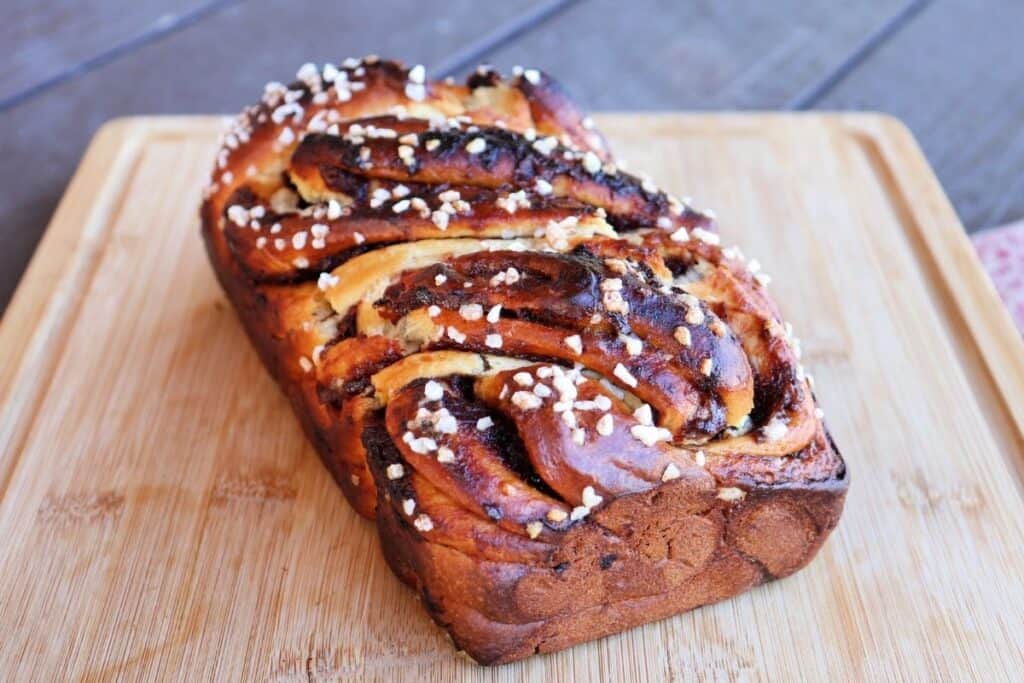 A loaf of jam filled bread sitting unsliced on a wooden cutting board.