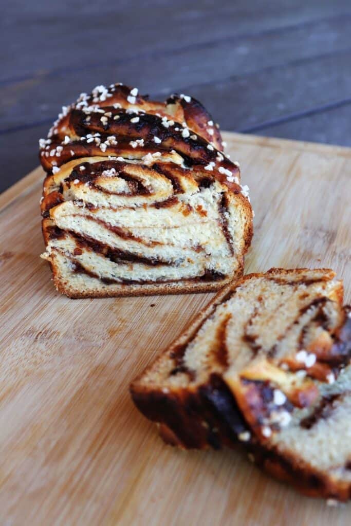 A loaf of jam filled bread sliced open exposing the bread and jam ribbons inside sitting on a wooden cutting board.