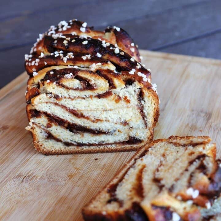 A sliced loaf of jam filled bread on a cutting board sitting behind slices of the bread.