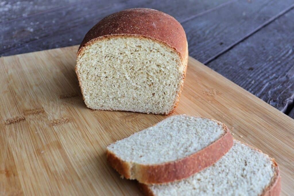 A loaf of bread with the end cut off sitting on a cutting board behind a few slices of bread.