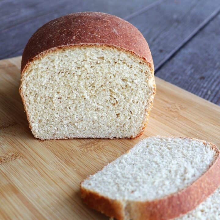 A loaf of bread with the end cut off sitting on a cutting board with slices of bread in front.