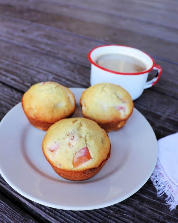 3 nectarine muffins on a plate with a white napkin sitting to the right and a cup of coffee in the background.
