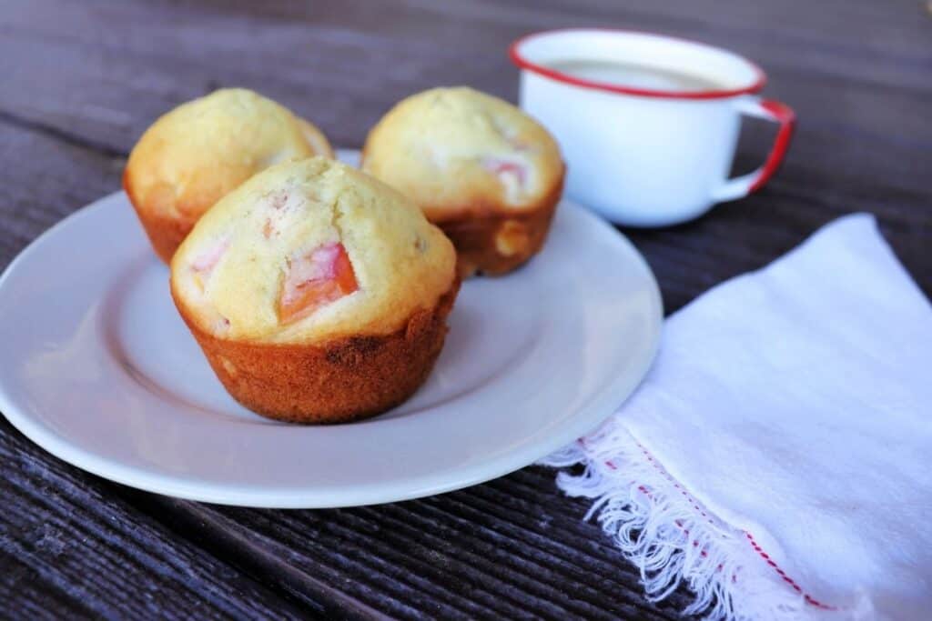 3 nectarine muffins on a plate with a white napkin sitting to the right and a cup of coffee in the background.