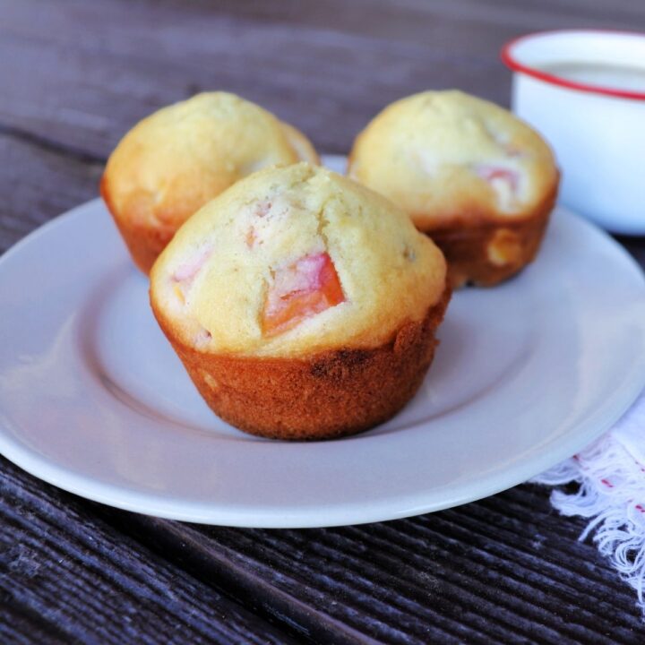 3 nectarine muffins on a plate with a white napkin sitting to the right and a cup of coffee in the background.