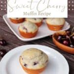 A muffin sitting on a white plate with a platter of more muffins in the background and a wooden bowl full of sweet cherries beside it with text overlay reading: sweet cherry muffin recipe.