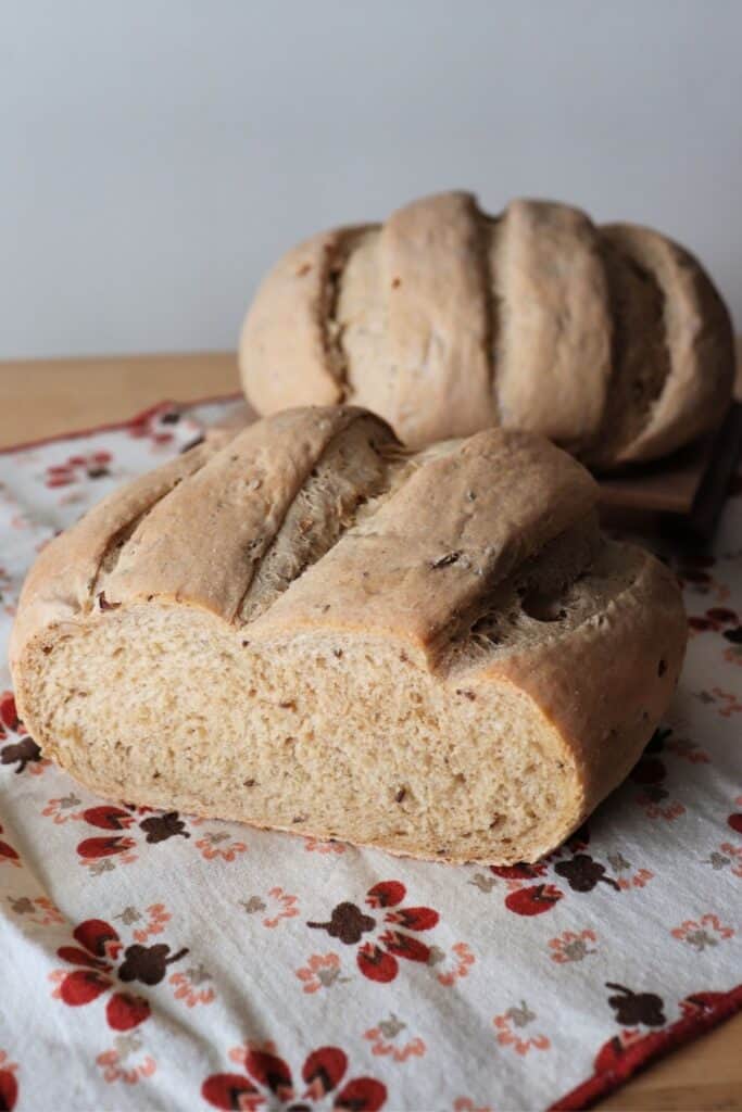 Two round loaves of sauerkraut rye bread sitting on a printed napkin. The loaf in front has the end cut off exposing the inside.