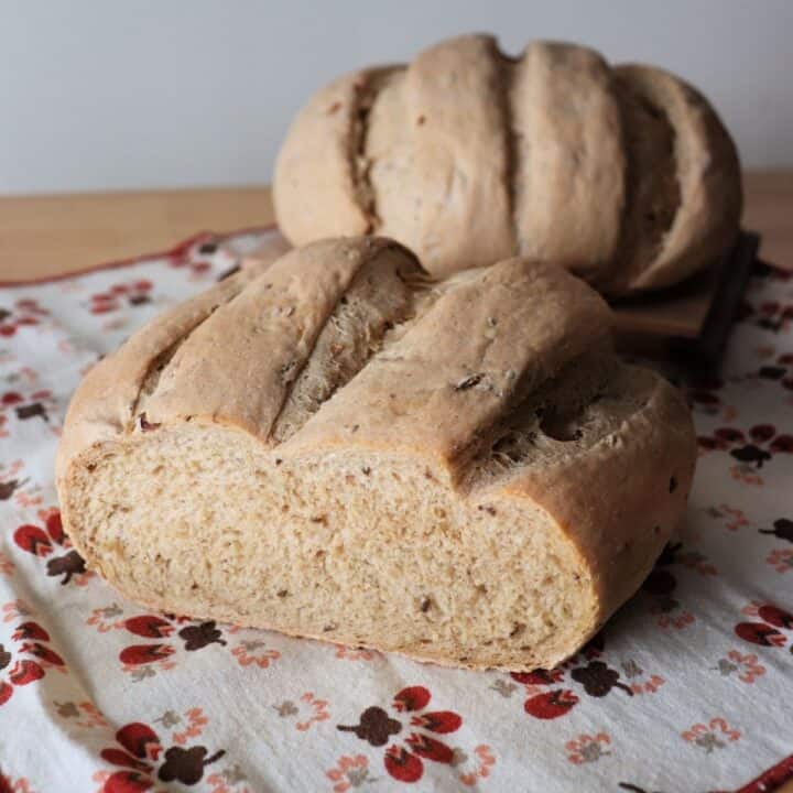 Two round loaves of sauerkraut bread sitting on a napkin, the loaf in front has the end cut off.