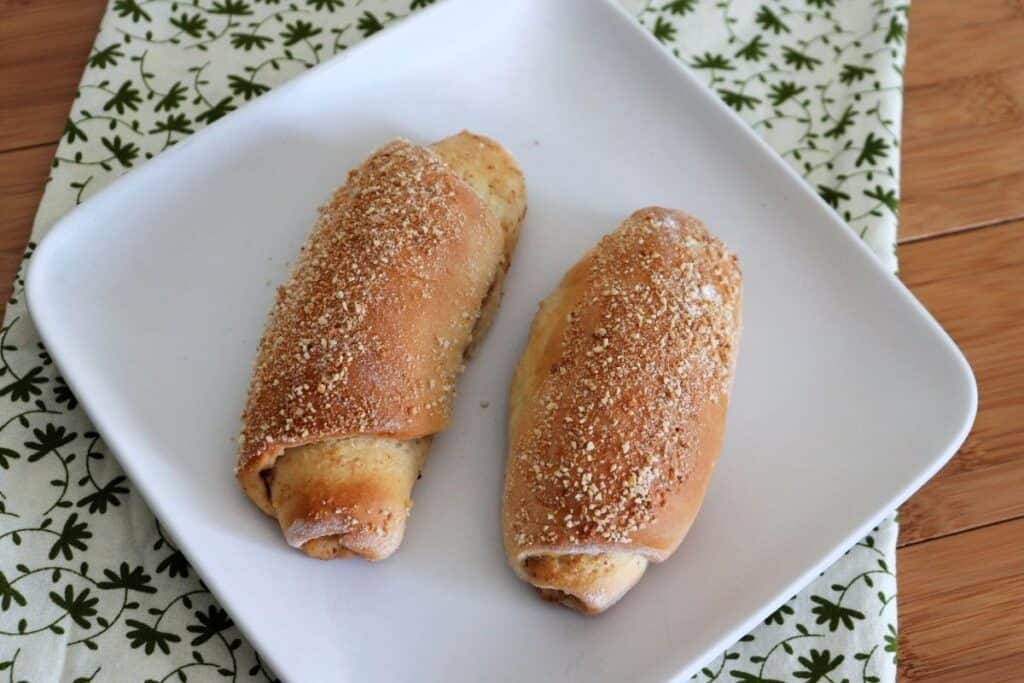 Two Señorita Bread rolls as seen from above sitting on a square white plate on top of a green and white cloth.