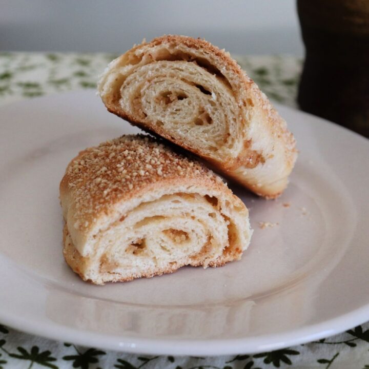 A senorita bread roll cut in half exposing layers inside sitting on a white plate.