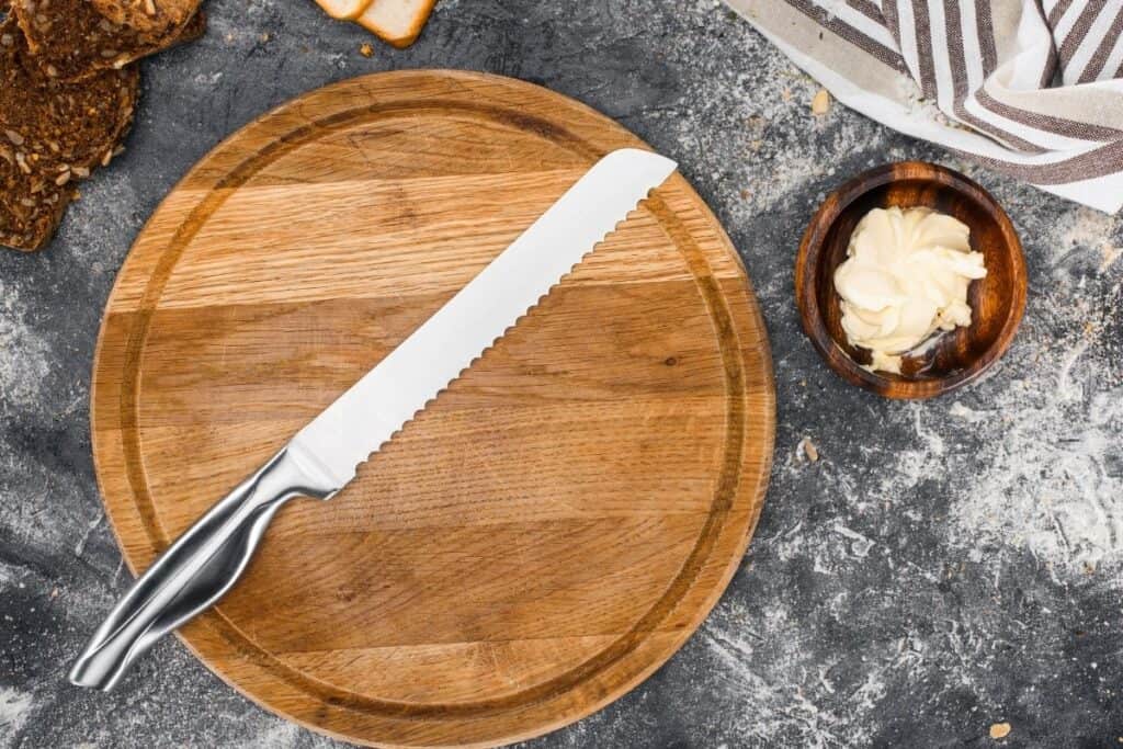 A bread knife sitting on a round cutting bowel with a bowl of butter sitting next to it.