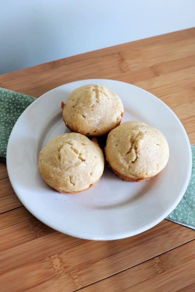 3 butter rum muffins as seen from above on a white plate that is sitting on a green cloth on a table.