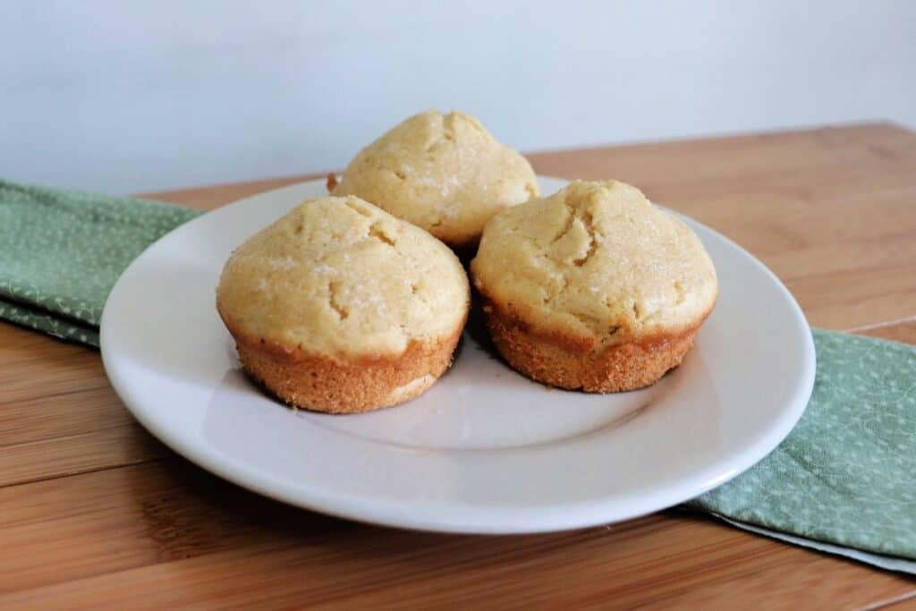 3 butter rum muffins on a white plate that is sitting on a green cloth on a table.