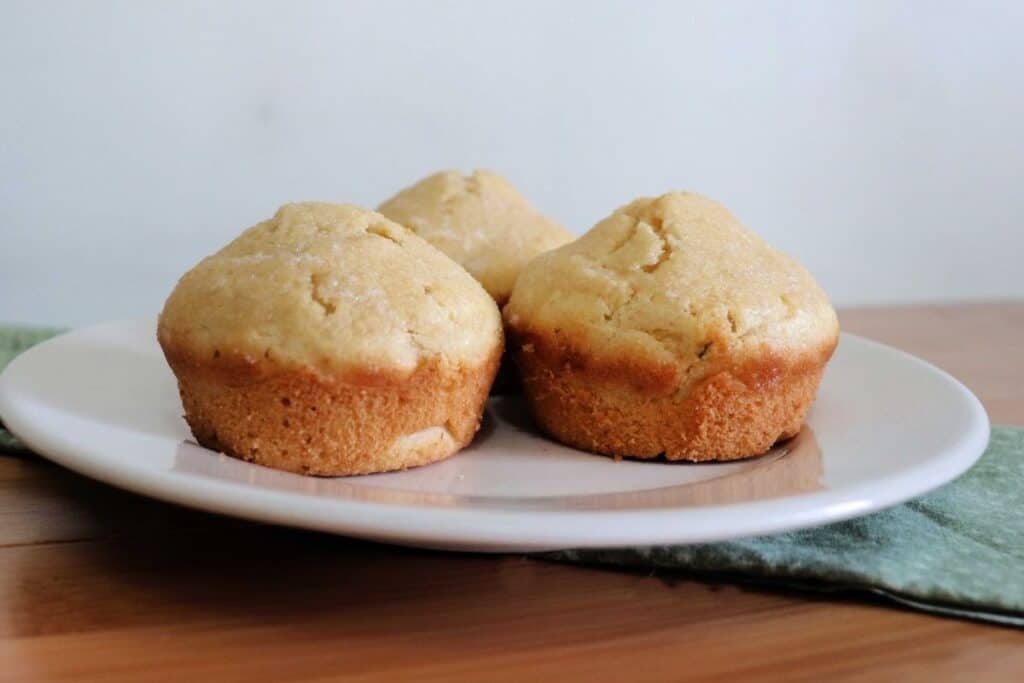 3 butter rum muffins on a white plate that is sitting on a green cloth on a table.