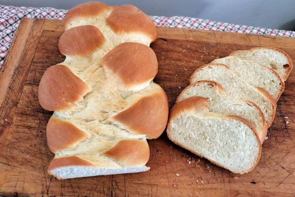 A braided loaf of bread sitting on a cutting board next to bread slices as seen from above.