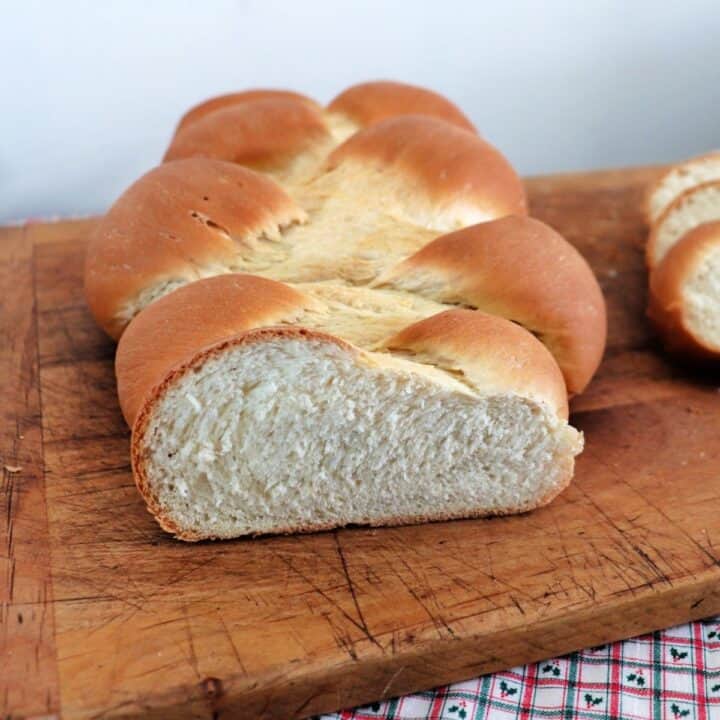 A braided loaf of white bread with the end cut off sitting on a cutting board.