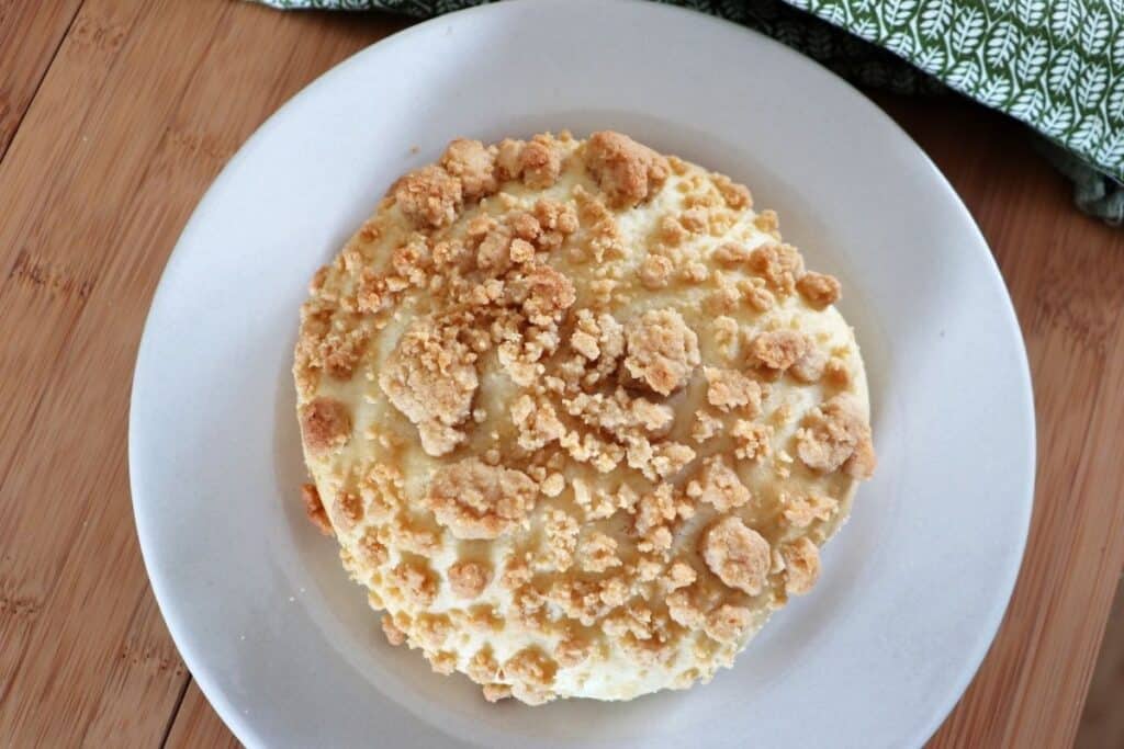 A streusel topped white bread roll sitting on a white plate with a green cloth behind it as seen from above.