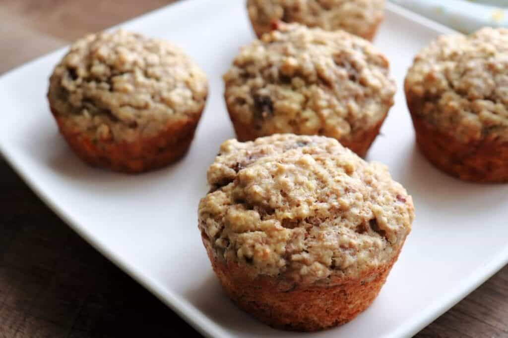 Banana bran muffins on a white plate sitting on wooden board.