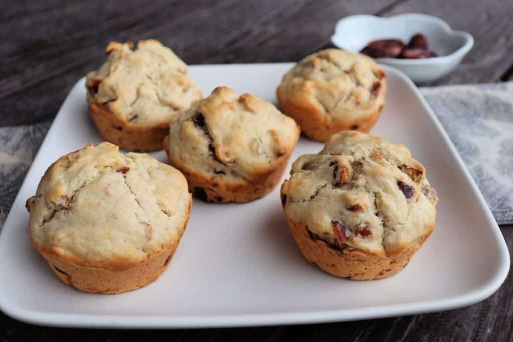 Date nut muffins on a square white plate with a bowl of dates in the background.