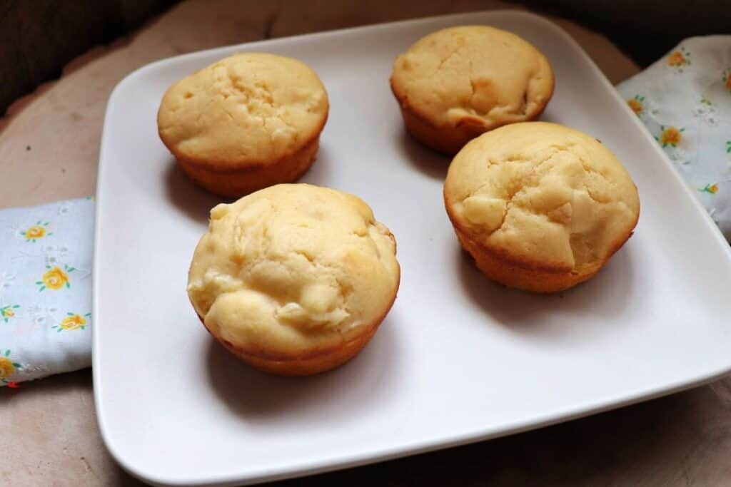 4 pineapple muffins on a square white plate sitting on top of a white and yellow cloth.