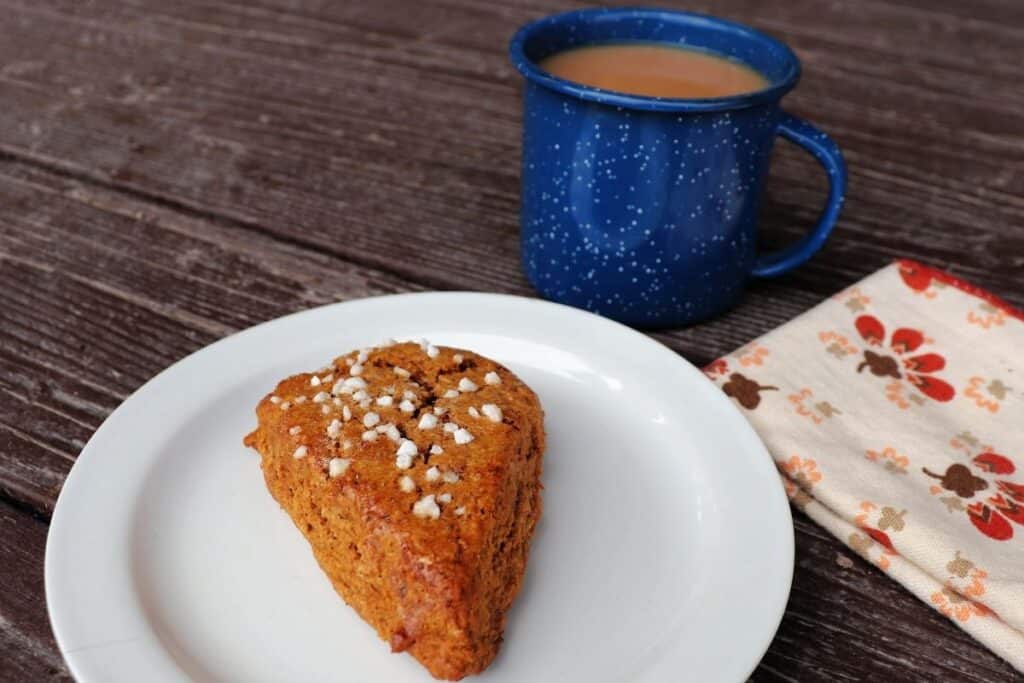 A gingerbread scone sitting on a plate with a napkin to the left and a blue cup with tea in it behind the plate.