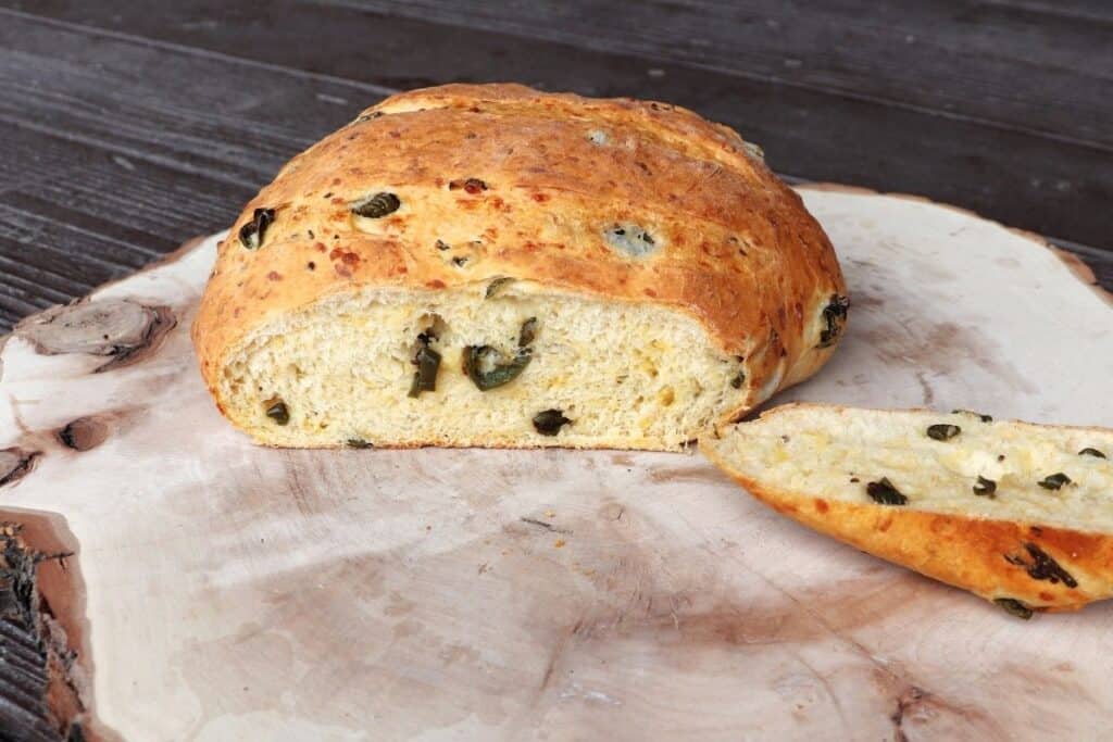 A loaf of jalapeno bread on a board with the end cut off exposing the cheese and jalapenos inside.