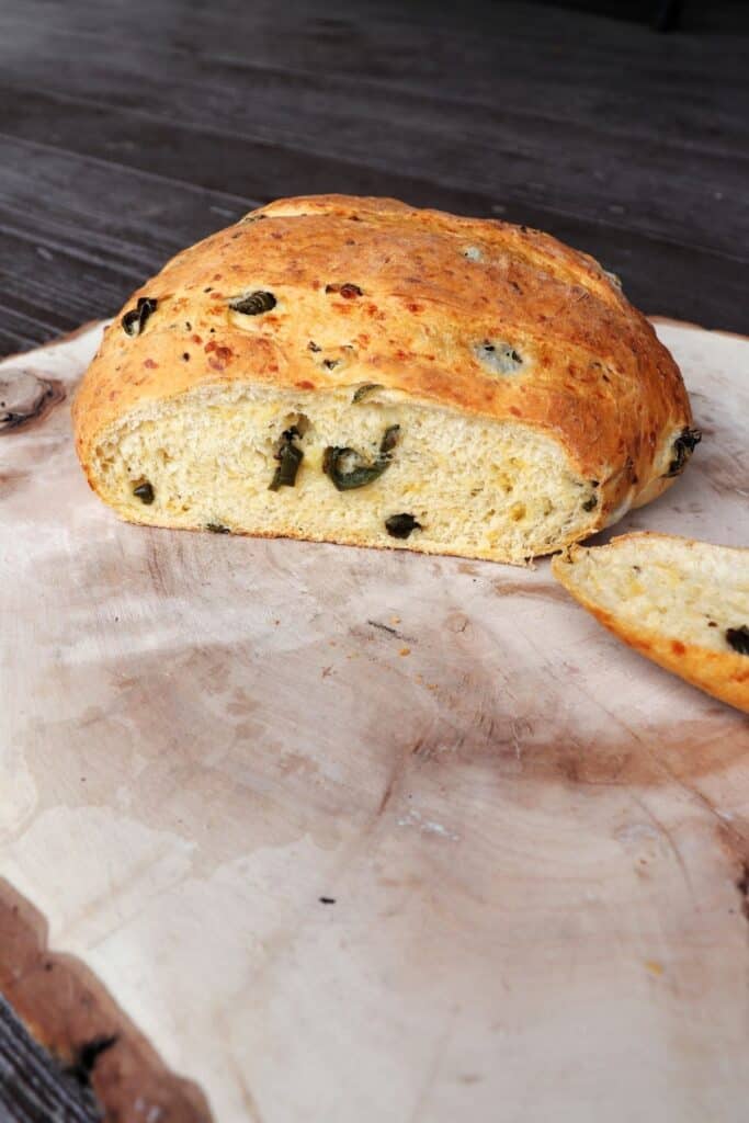 A loaf of jalapeno bread on a board with the end cut off exposing the cheese and jalapenos inside.