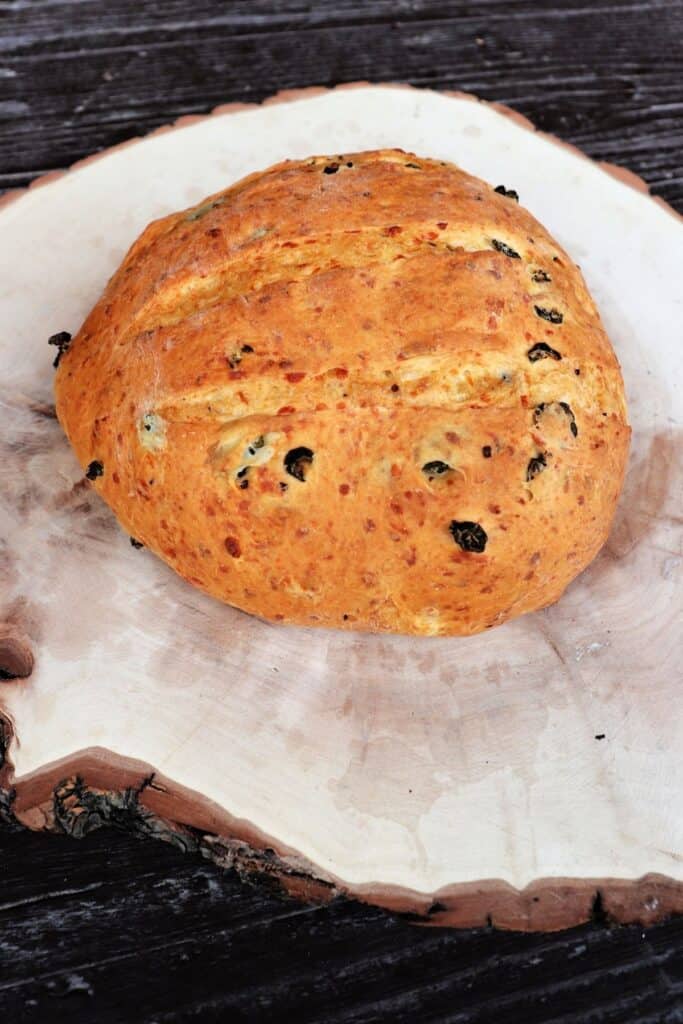 A loaf of bread studded with green peppers on a board.