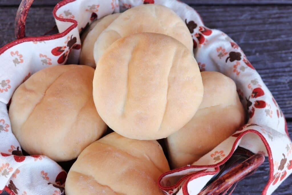 A close up of the indents on a telera roll sitting on top of other rolls in a linen lined basket.