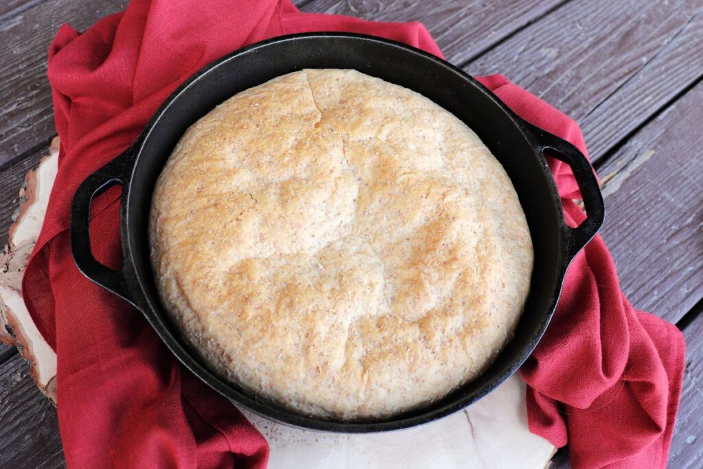 A loaf of shepherd's bread sitting in a black cast iron Dutch oven surrounded by a red cloth as seen from above.