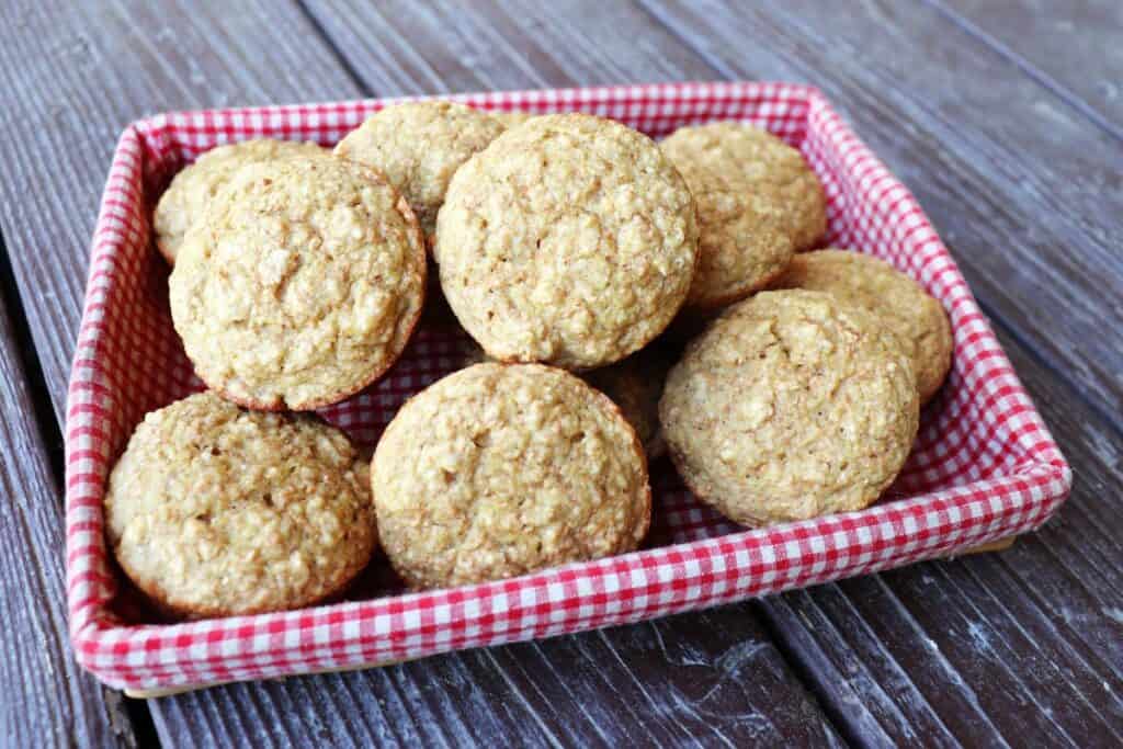 Applesauce bran muffins stacked in a basket lined with a red and white checkered cloth. 
