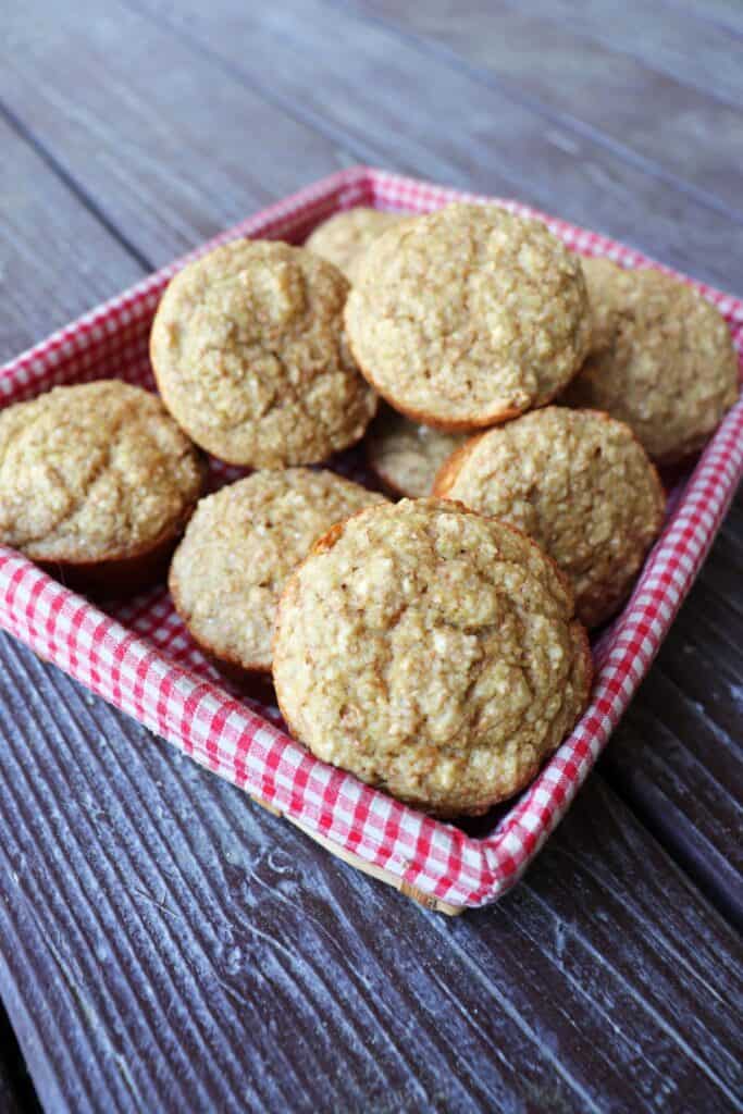 Applesauce bran muffins stacked in a basket lined with a red and white checkered cloth. 
