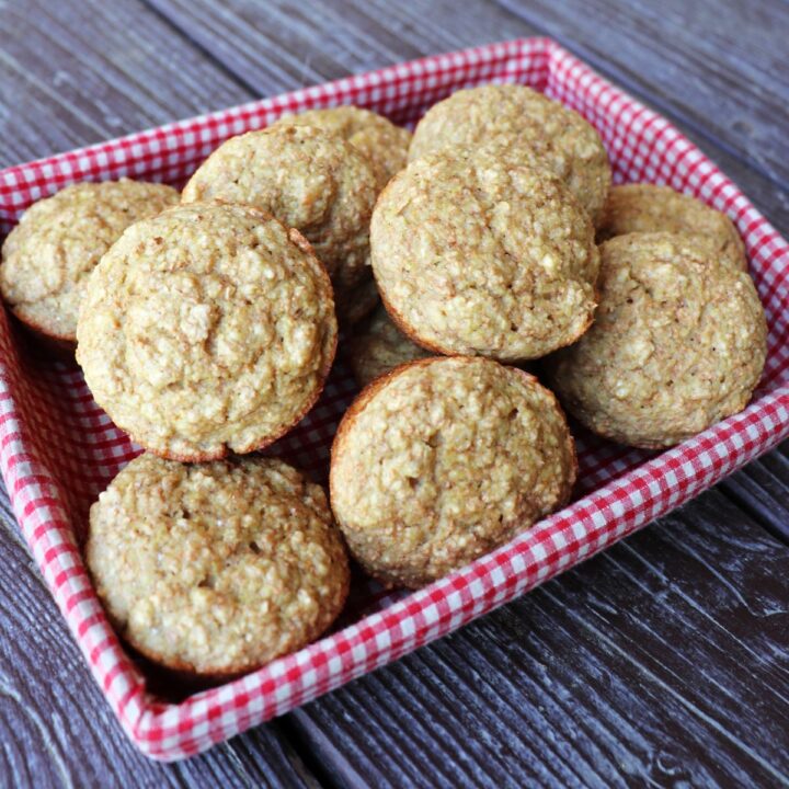 Applesauce bran muffins stacked in a basket lined with a red and white checkered cloth.