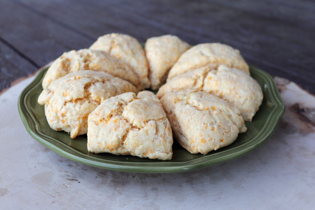 A ring of 8 triangle shaped scones sitting on a green plate on top of a wooden board.