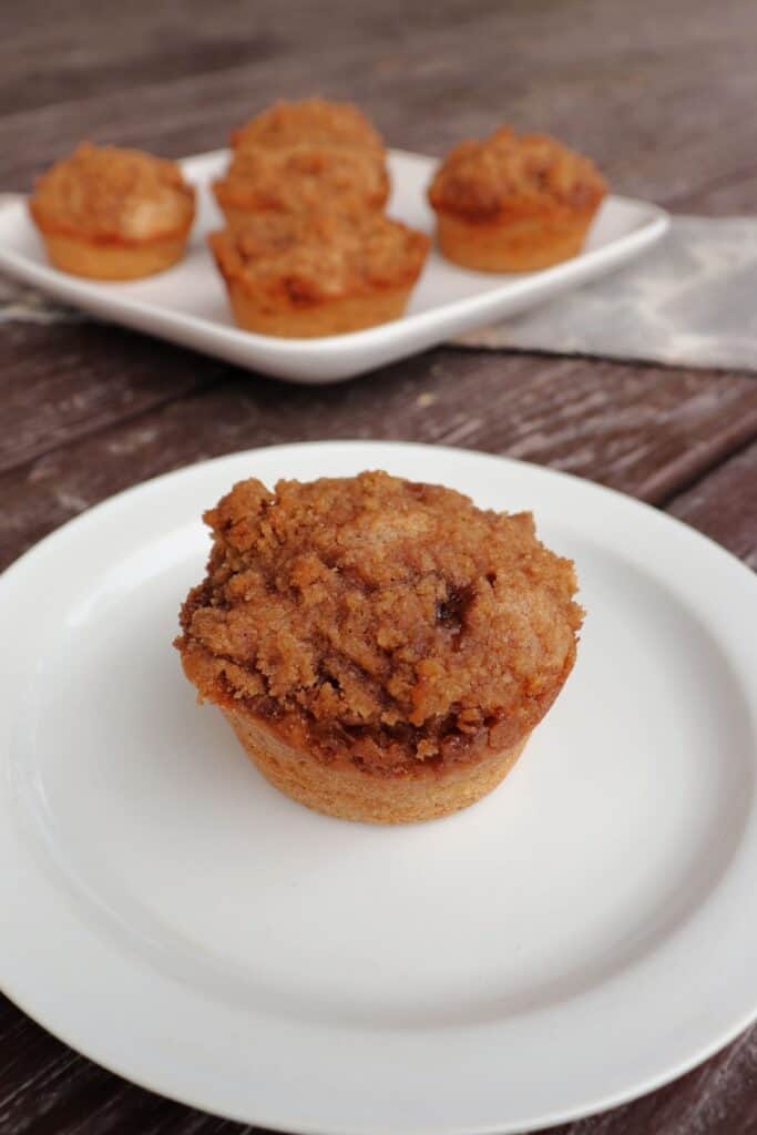 A cinnamon muffin on a plate as seen from above with a platter of more muffins in the background.