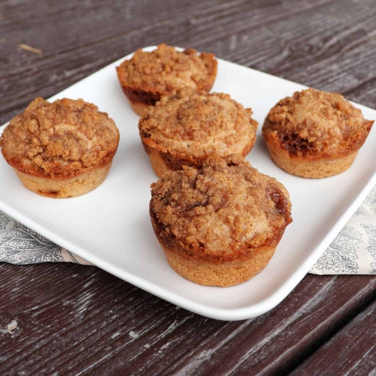 5 cinnamon muffins on a square white plate.