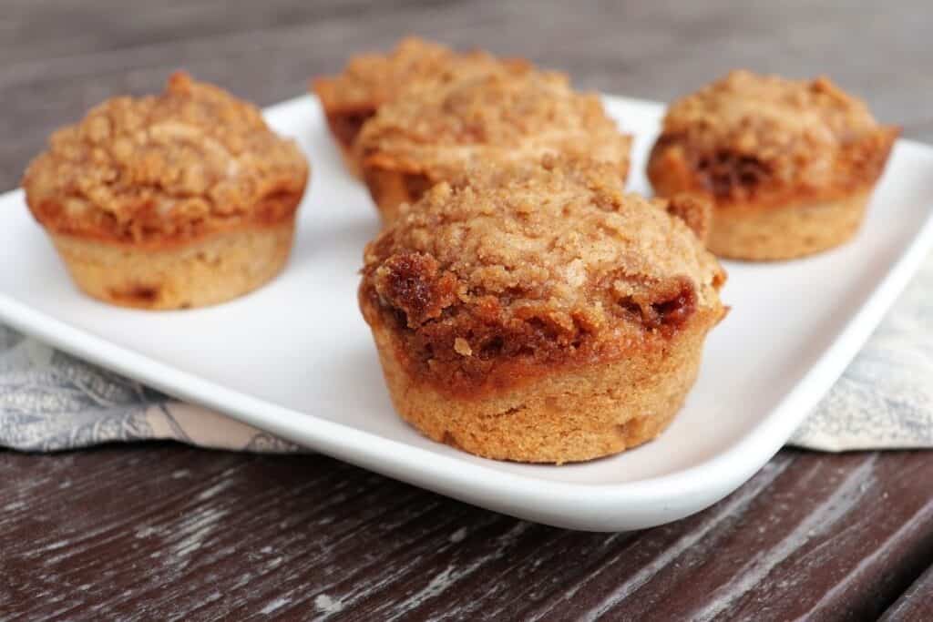 Close up of edge of cinnamon muffin on a square white plate with more muffins.