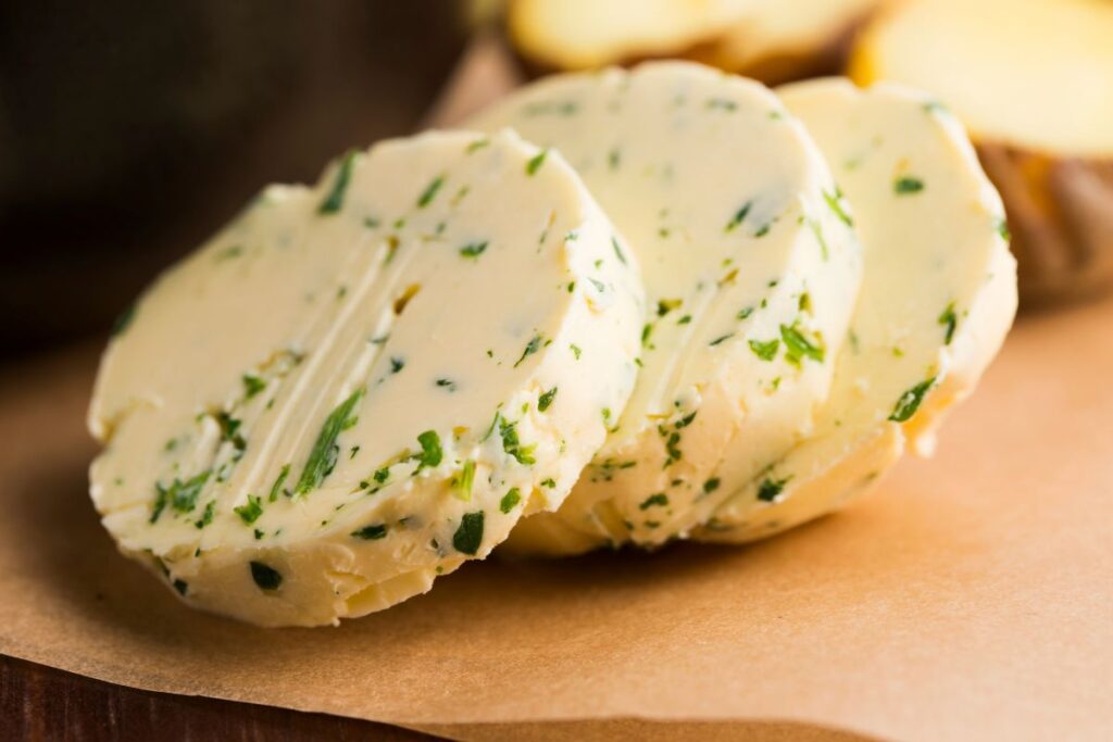 Slices of round herb infused butter sitting on parchment paper.