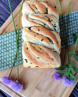 Fresh herb bread as seen from above sitting on a green cloth surrounded by fresh herbs.