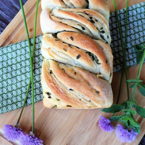 Fresh herb bread as seen from above sitting on a green cloth surrounded by fresh herbs.